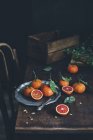 Цельные и вдвое свежие спелые мандарины с листьями на темном деревянном столе — стоковое фото