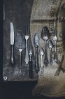 Vintage silver kitchen cutlery on sackcloth on shabby rustic table — Stock Photo