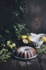 Lemon bundt cake with icing sugar on wooden table with flowers — Stock Photo