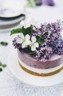 Bolo de queijo de mirtilo e baunilha decorado com flores lilás frescas na mesa de jardim — Fotografia de Stock