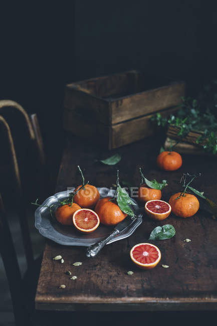 Mandarinas maduras frescas enteras y cortadas a la mitad con hojas sobre una mesa de madera oscura - foto de stock