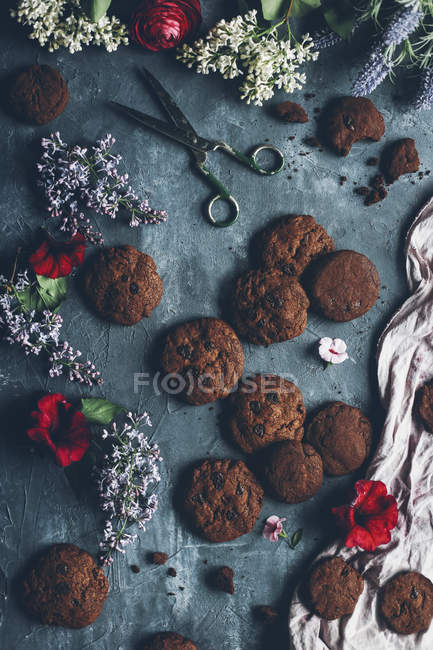 Gebackene Schokoladenkekse auf grauer schäbiger Oberfläche mit Blüte und Schere — Stockfoto