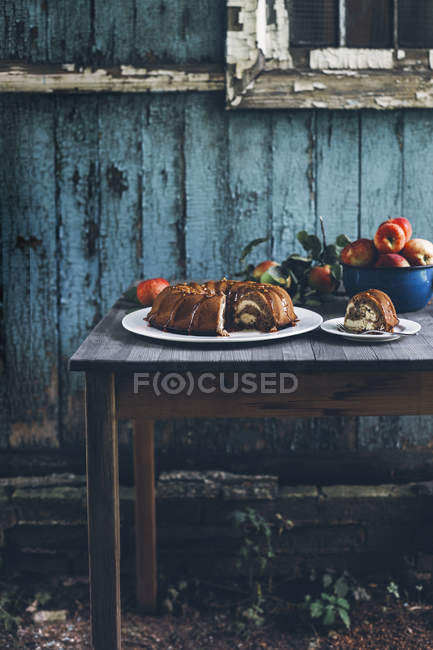Apple bundt cake with cream cheese filling on wooden table in front of old house — Stock Photo