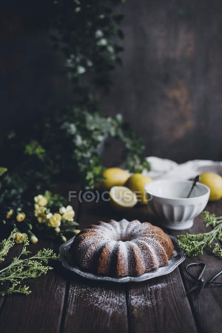 Lemon bundt cake with icing sugar on wooden table with flowers — Stock Photo