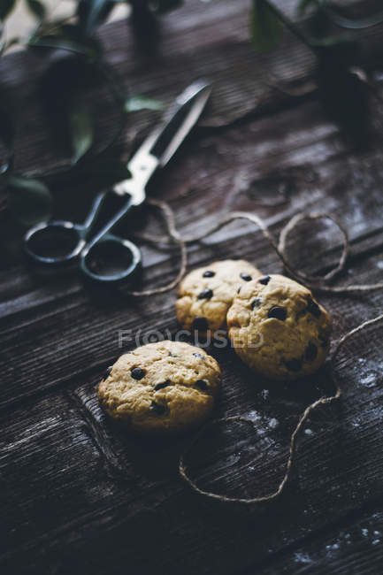 Печенье с шоколадной крошкой на деревянной поверхности с бечевкой и ножницами — стоковое фото
