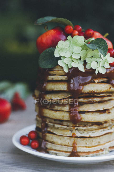 Stacked pancakes with berries and fruit jam on plate on garden table — Stock Photo