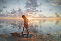 Дівчина блукає в океанічному серфінгу на спокійному пляжі заходу сонця — стокове фото