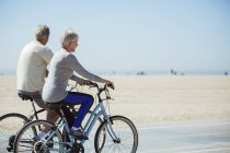 Couple aîné à vélo sur la plage — Photo de stock
