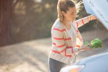 Mulher verificando o óleo sob o capuz do automóvel na estrada — Fotografia de Stock