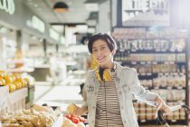 Portrait souriant, confiant jeune femme avec écouteurs épicerie shopping dans le marché — Photo de stock