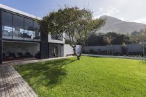 Sunny home showcase exterior lawn and tree below mountain — Stock Photo