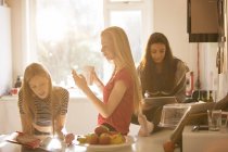 Teenage girls reading magazine, texting and using digital tablet in kitchen — Stock Photo