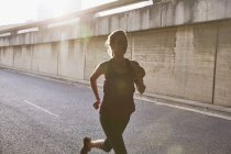 Silueta corredor femenino corriendo en la soleada calle urbana - foto de stock