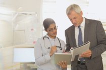 Médica e administradora do hospital conversando, olhando para tablet digital e papelada na sala de exame — Fotografia de Stock