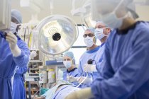 Médecins effectuant une chirurgie en salle d'opération, en regardant moniteur — Photo de stock