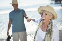 Entusiasta coppia di anziani che si tiene per mano sulla spiaggia soleggiata — Foto stock