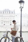 Empresário usando celular em bicicleta ao longo do Rio Sena, Paris, França — Fotografia de Stock