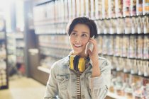 Smiling young woman with headphones talking on cell phone in grocery store market — Stock Photo
