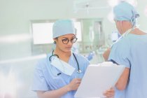 Chirurgin überprüft Papierkram auf Klemmbrett im Operationssaal — Stockfoto