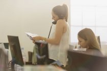 Бізнес-леді з паперовими роботами розмовляють по телефону в офісі — стокове фото