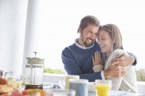 Sonriente pareja cariñosa abrazándose en el patio mesa de desayuno - foto de stock