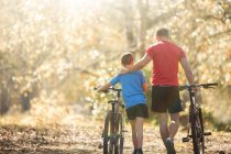 Affectionate father and son walking mountain bikes on path in woods — Stock Photo