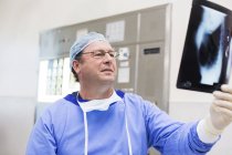 Arzt mit OP-Mütze und Kittel schaut sich Röntgenbild im Operationssaal an — Stockfoto
