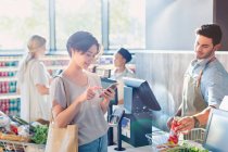 Young woman using cell phone at grocery store market checkout — Stock Photo