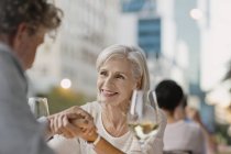 Любящие пожилые пары держатся за руки и пьют белое вино в городском кафе на тротуаре — стоковое фото