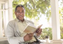 Portrait of smiling senior man reading book on porch — Stock Photo