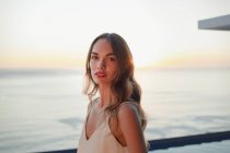 Retrato sério, bela mulher no pátio de luxo com vista para o mar por do sol — Fotografia de Stock