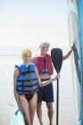 Portrait of senior couple with paddleboards on beach — Stock Photo