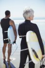Visão traseira do casal sênior com pranchas de surf na praia — Fotografia de Stock