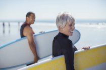 Coppia di anziani che trasportano tavole da surf sulla spiaggia — Foto stock