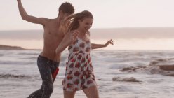 Juguetona pareja joven corriendo en la playa - foto de stock