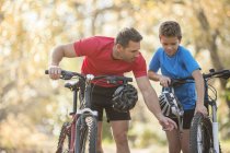 Padre e hijo examinando rueda en bicicleta de montaña - foto de stock