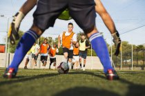 Vue à travers les jambes de gardien de but pour les joueurs de football s'entraînant sur le terrain — Photo de stock
