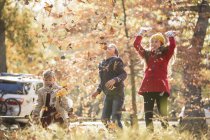 Boys and girl throwing autumn leaves overhead — Stock Photo
