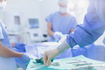 Chirurg in Gummihandschuhen greift nach Chirurgenschere auf Tablett im Operationssaal — Stockfoto