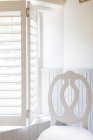 Cadeira por janela com persianas de madeira — Fotografia de Stock