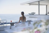 Donna serena meditando su moderno, lusso casa vetrina patio esterno con vista sull'oceano — Foto stock