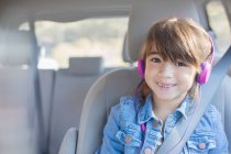 Портрет улыбающейся девушки с наушниками на заднем сиденье автомобиля — стоковое фото