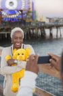 Senior woman with teddy bear posing for photograph at amusement park — Stock Photo
