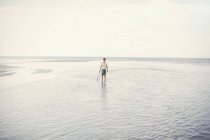 Porträt Junge hält Schubser in der Brandung des Meeres am bewölkten Sommerstrand — Stockfoto