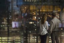 Businessman and businesswoman looking out urban office window at night — Stock Photo