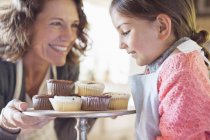 Happy grandmother offering granddaughter cupcakes — Stock Photo