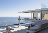 Frau auf sonnigem, modernem, luxuriösem Haus Vitrine Außenterrasse mit Meerblick — Stockfoto