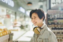 Smiling young woman with headphones grocery shopping in market — Stock Photo