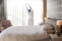 Donna in accappatoio che si estende con le braccia alzate in camera da letto — Foto stock