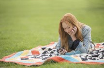 Жінка використовує мобільний телефон на ковдрі в парку — стокове фото